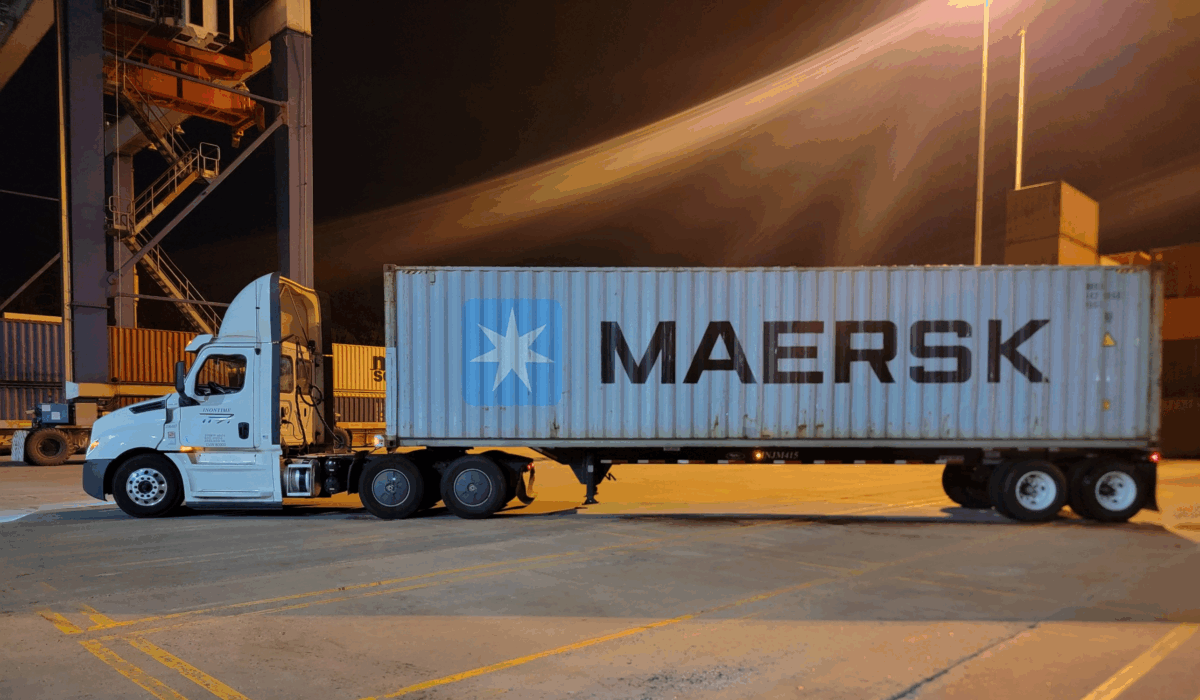 Greer Container Truck An Inontime semi-truck hauling a Maersk container at night inside a well-lit port terminal.