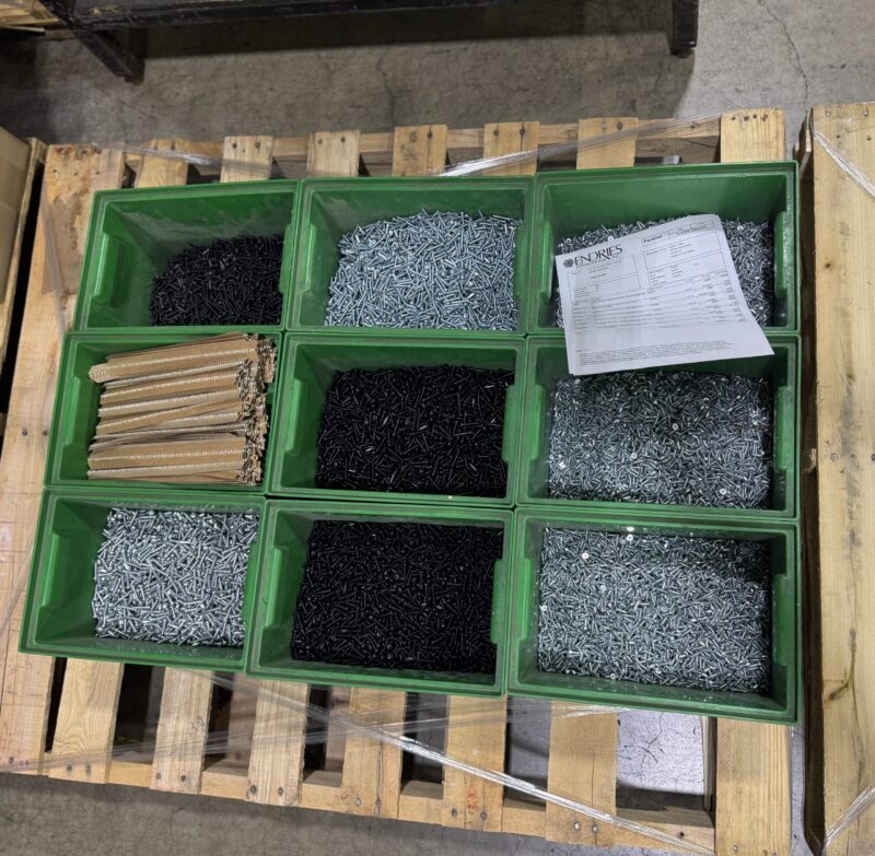sequencing-hardware-production-line Green bins filled with sorted hardware parts and instructions, staged on a pallet for production line sequencing.