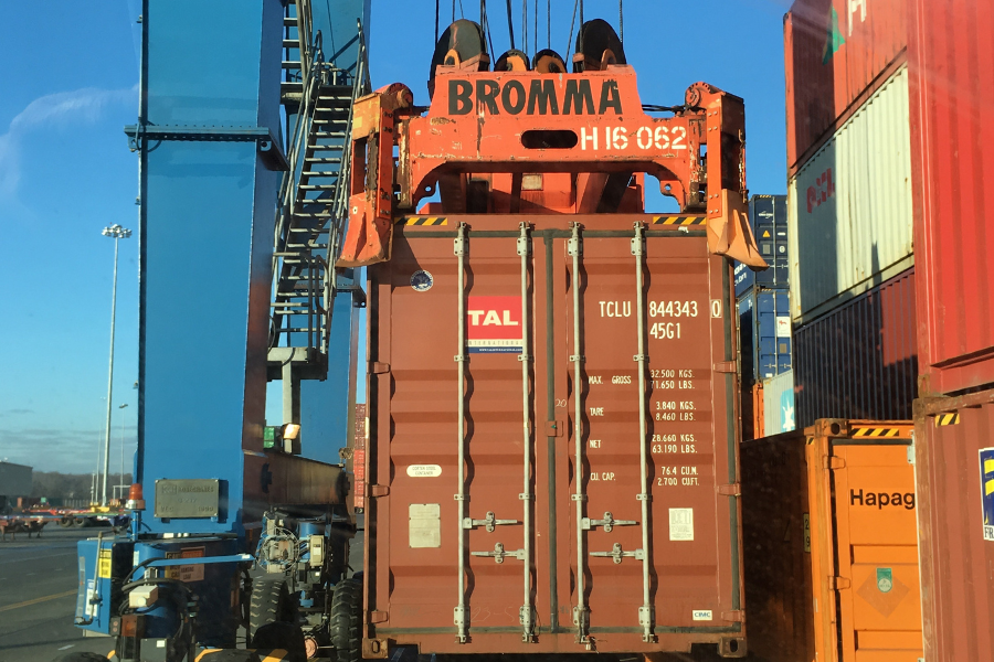 4 Two Inontime semi-trucks facing each other at a port terminal, surrounded by stacks of colorful shipping containers.
