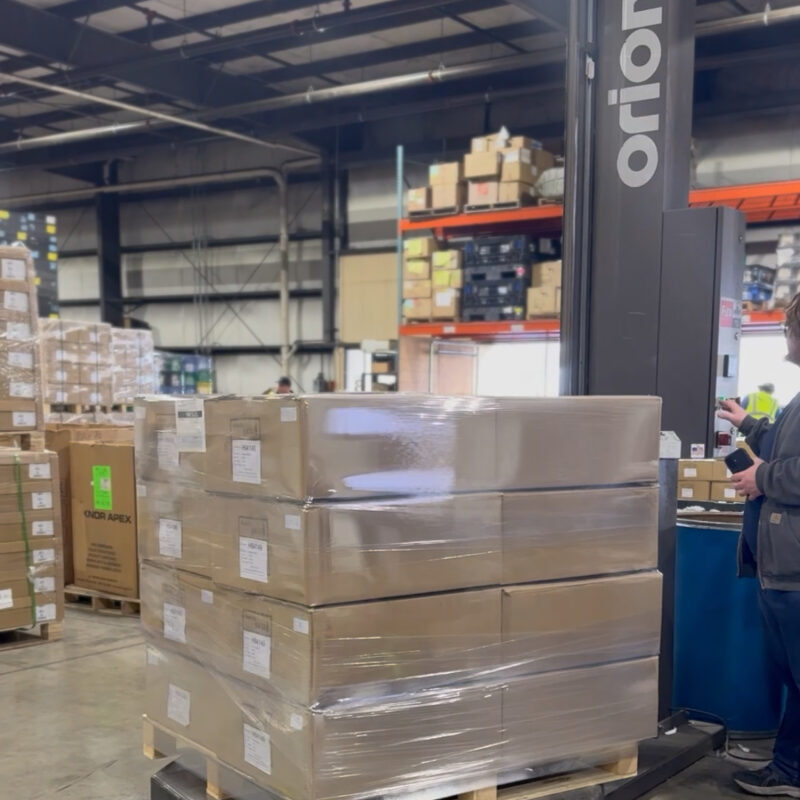 IMG_4782 Pallet of boxed goods being wrapped with stretch film on an automated wrapping machine in a warehouse.
