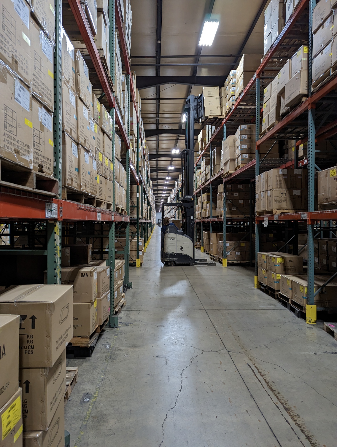 Long warehouse aisle with tall pallet racking stacked with uniformly labeled boxes.
